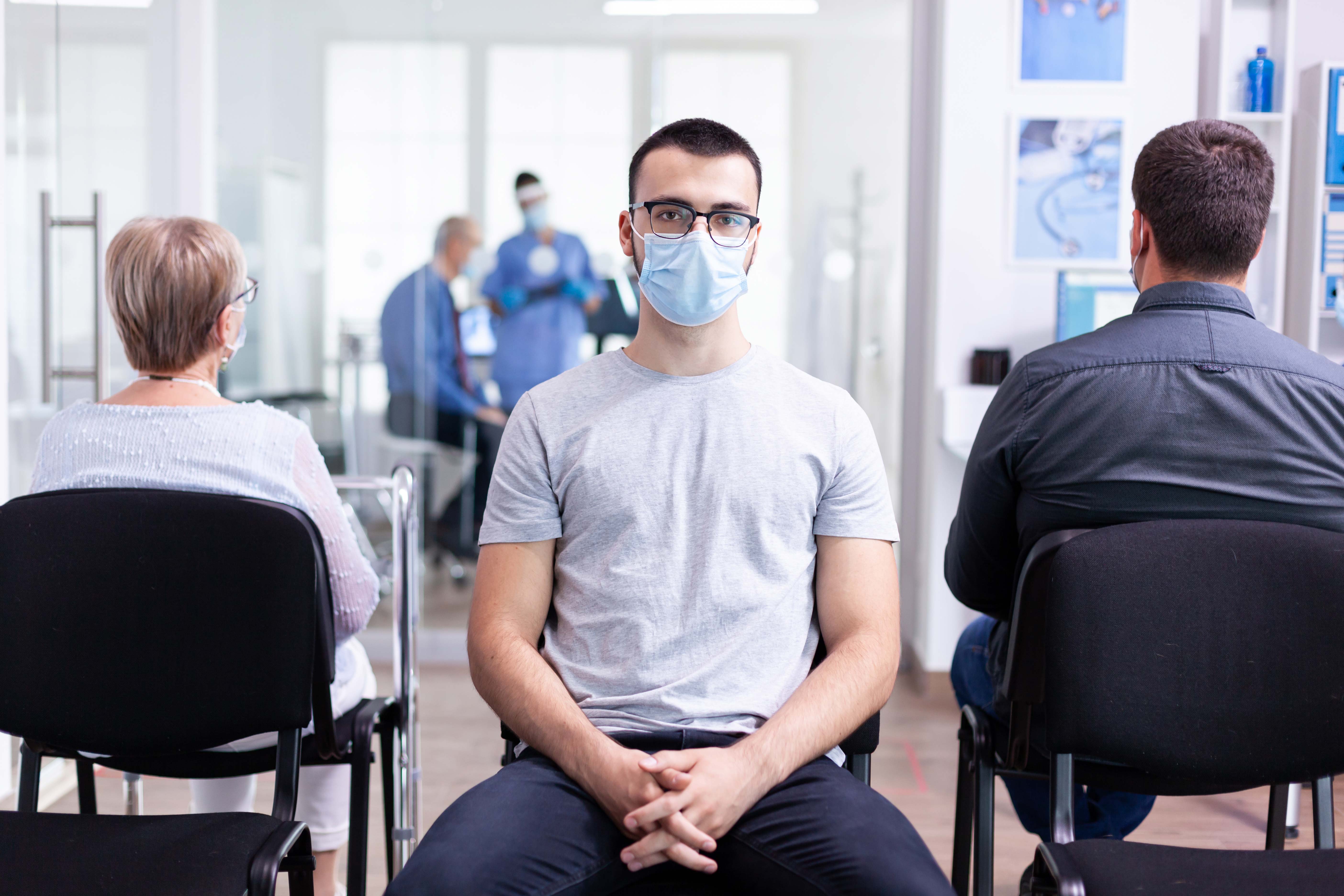 portrait tired young man with face mask against coronavirus hospital waiting area looking camera